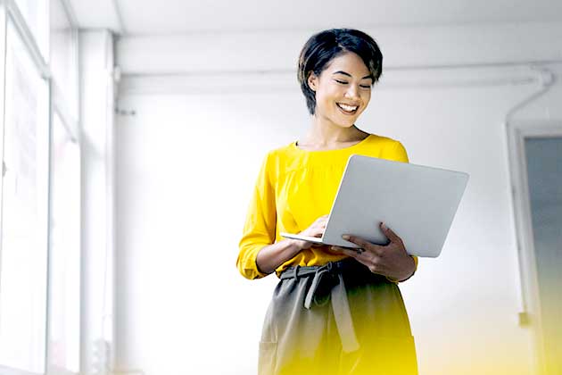 woman in a yellow shirt holding a laptop and smiling